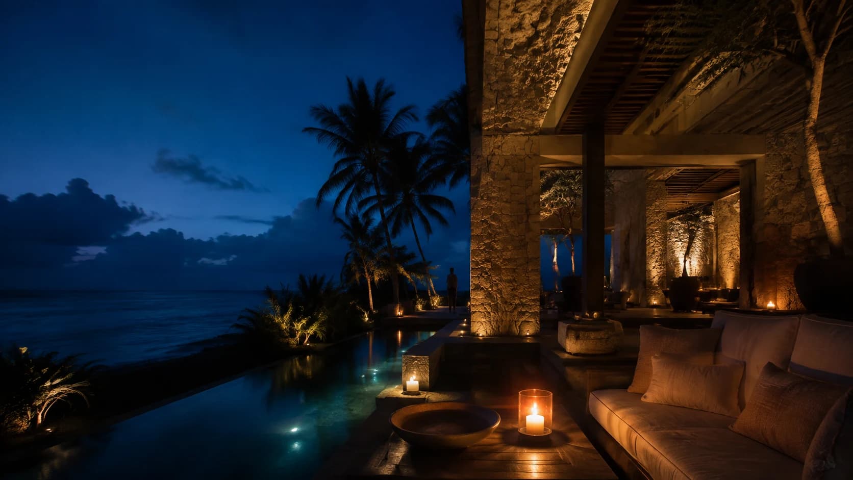 A candlelit hotel terrace and long pool beside the Caribbean at blue hour